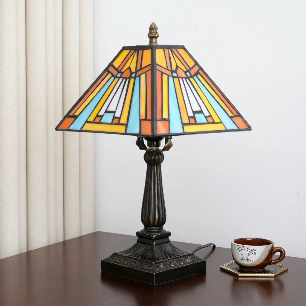 Pyramid lamp on a table next to a teacup, curtains behind