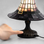 A finger on the base of the witch hat lamp, showing the carved stand and the cord