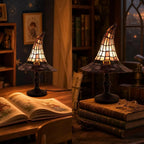 Two witch hat lamps lit on a desk and a stack of old books in a dim study