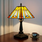 Stained glass pyramid lamp lit on a dark wood table, amber and sky-blue panels, warm glow on the wall